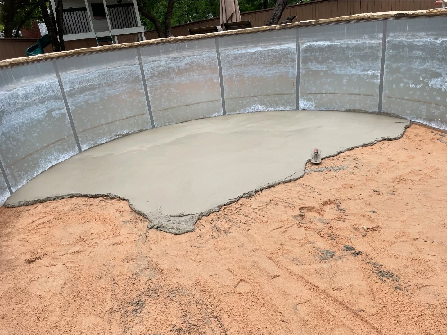 Fresh concrete poured in a curved swimming pool under construction, surrounded by sandy ground