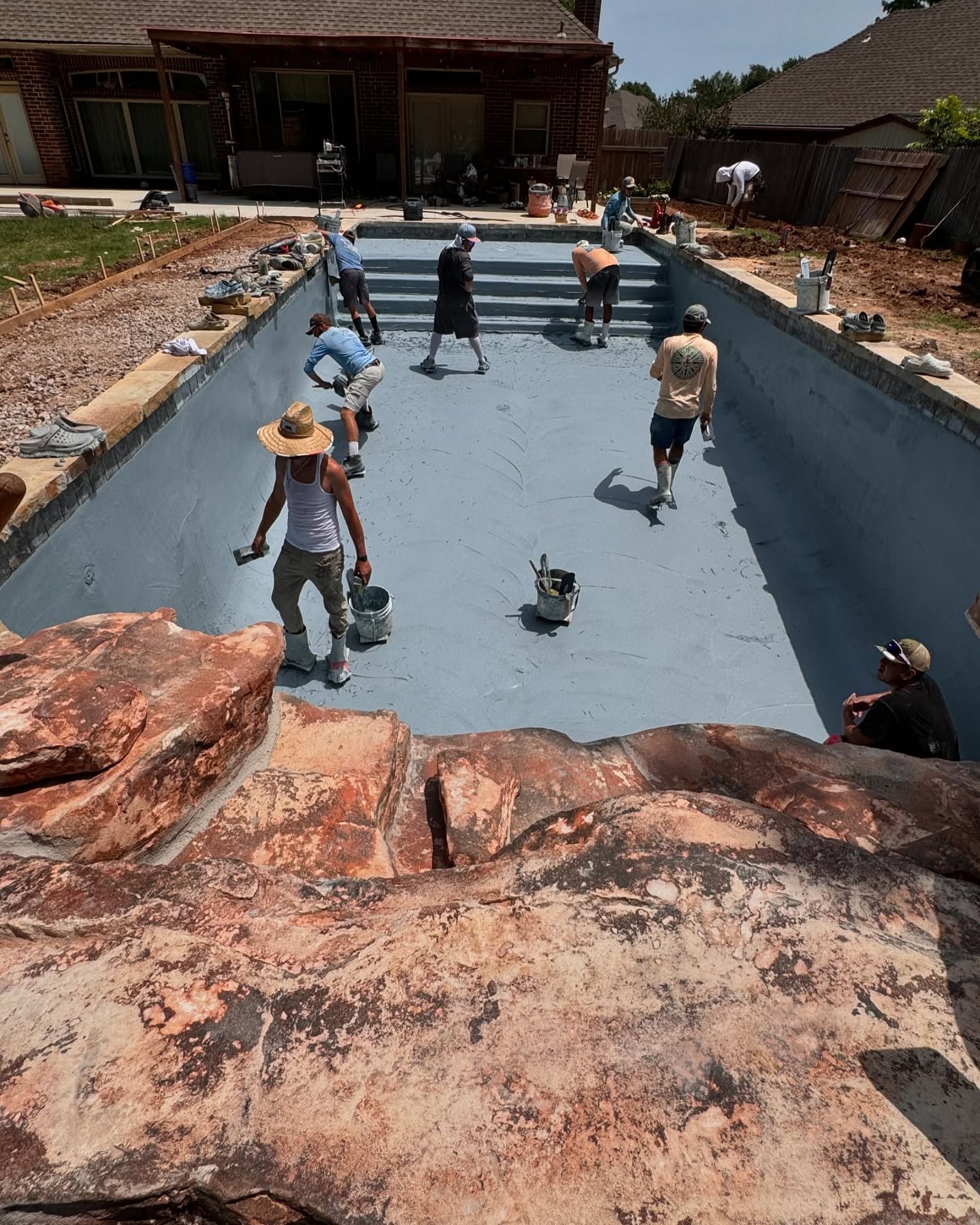 Empty swimming pool under repair with workers and tools in a sunny courtyard