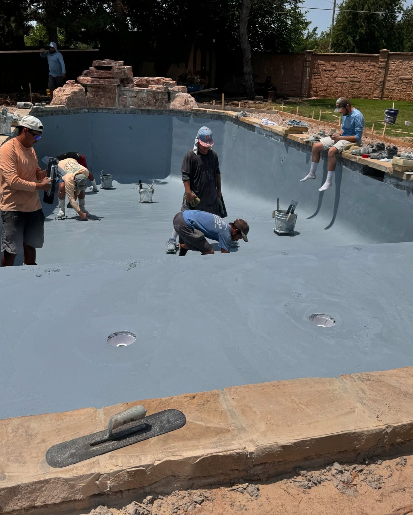 Workers installing a smooth blue liner in an empty backyard swimming pool.