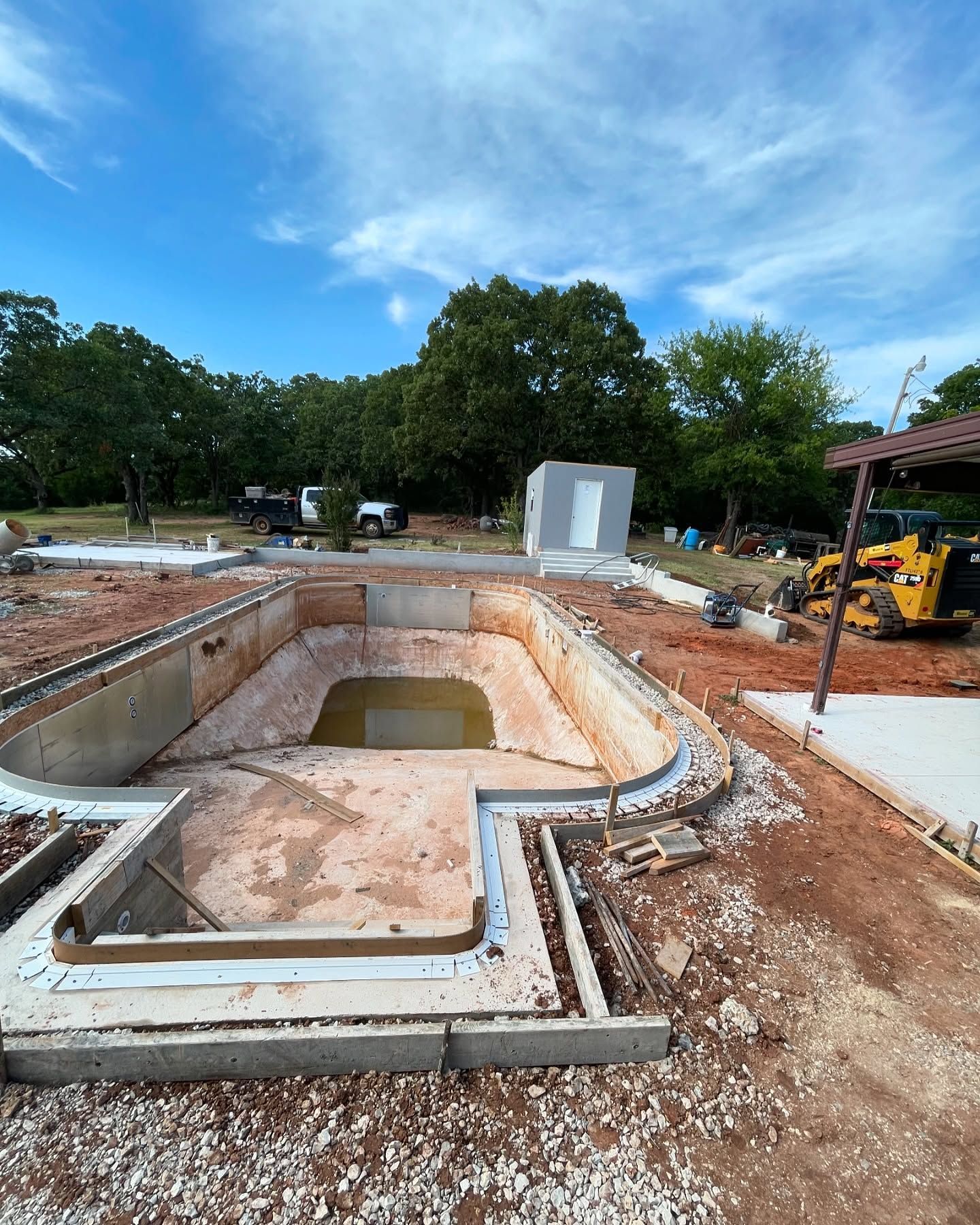 Empty backyard pool under construction with exposed concrete, dirt, and construction equipment nearby