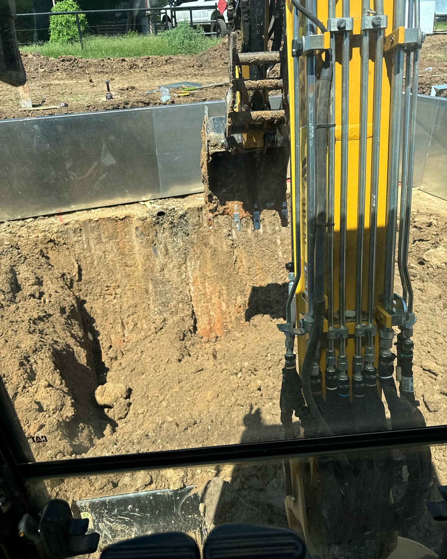 Yellow construction machinery digging a deep trench beside steel retaining walls at a work site
