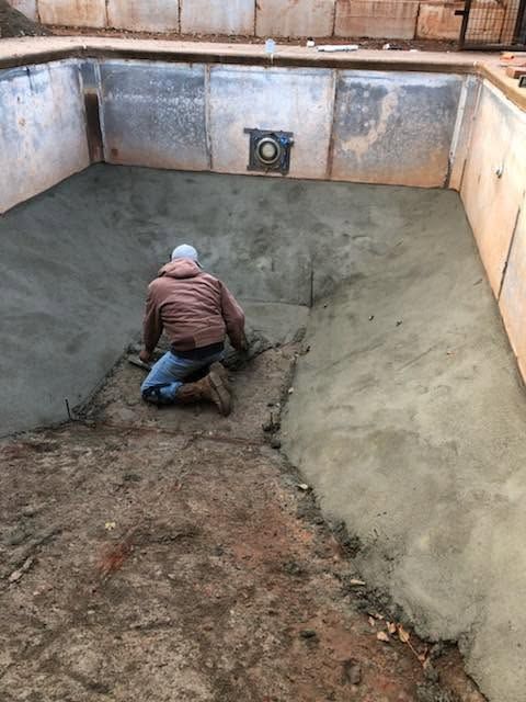 Worker smoothing concrete in an empty rectangular pool or basin