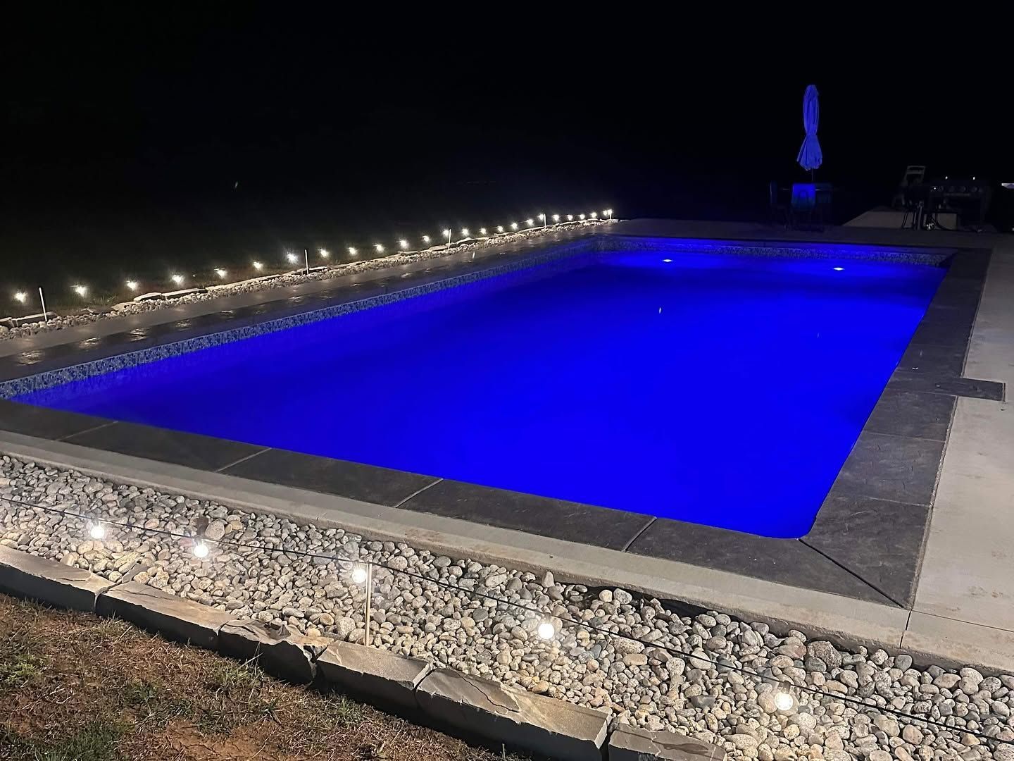 Blue-lit outdoor swimming pool at night with lights along the edge