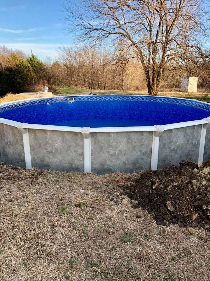 Above-ground pool with a blue cover in a backyard, surrounded by leafless trees and grass