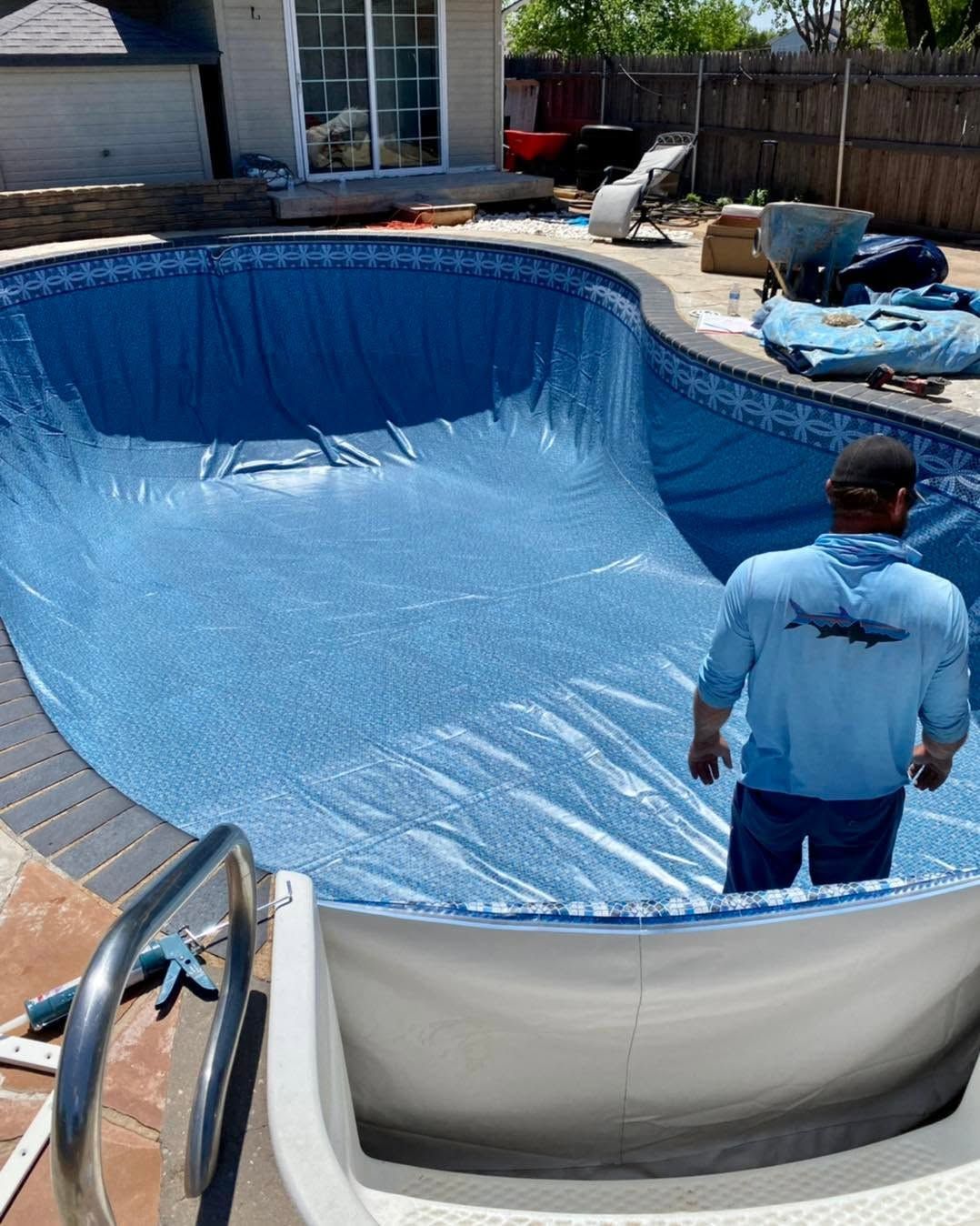 Above-ground pool being lined with blue material while a person stands inside the empty pool in a backyard.