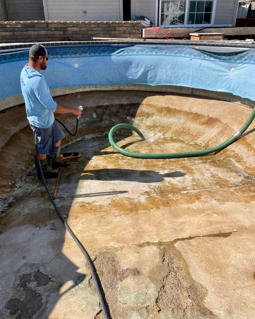 Worker cleaning an empty swimming pool with a hose and pressure washer
