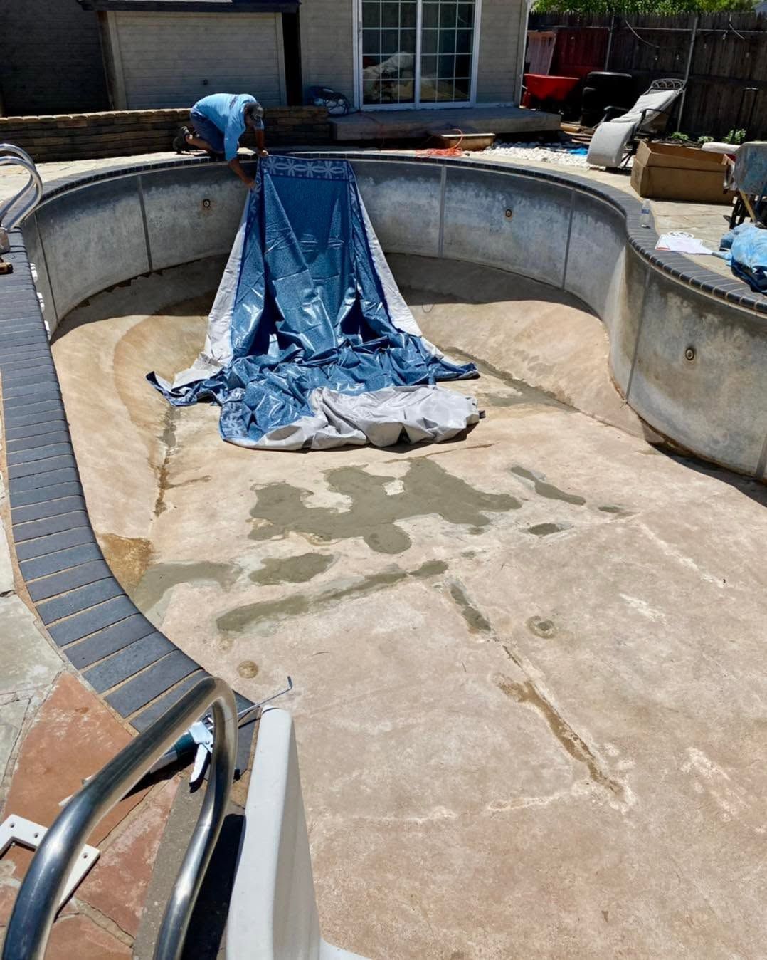 Empty drained pool with a blue tarp in the center and a person working on the far side.