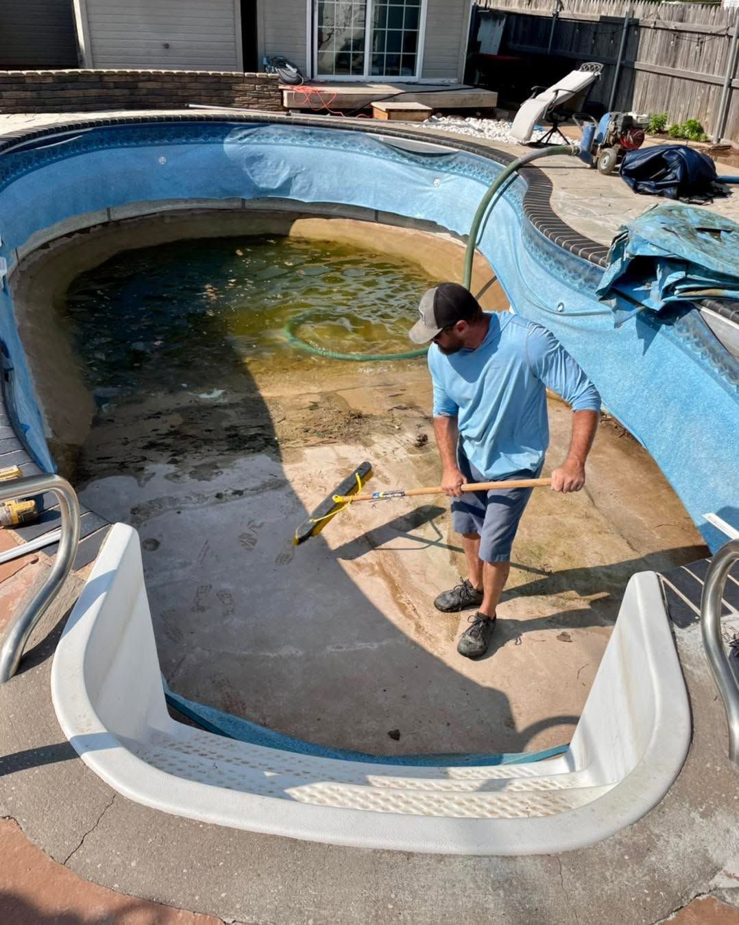 Person cleaning a drained swimming pool with a hose and tools.