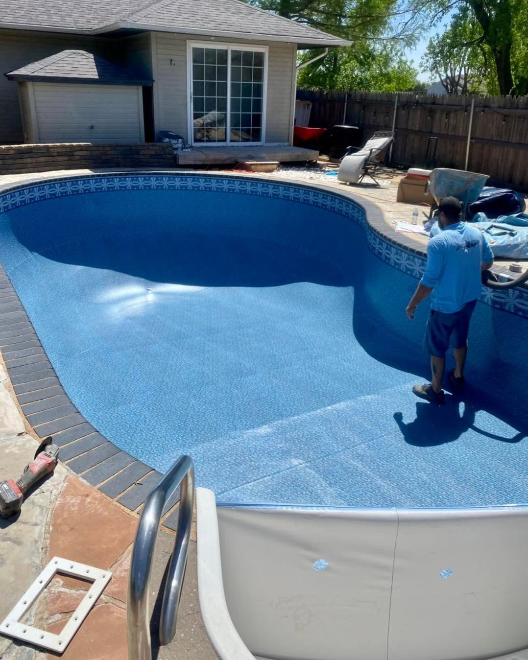 A backyard swimming pool with a child standing on the deck beside blue water and lounge chairs.