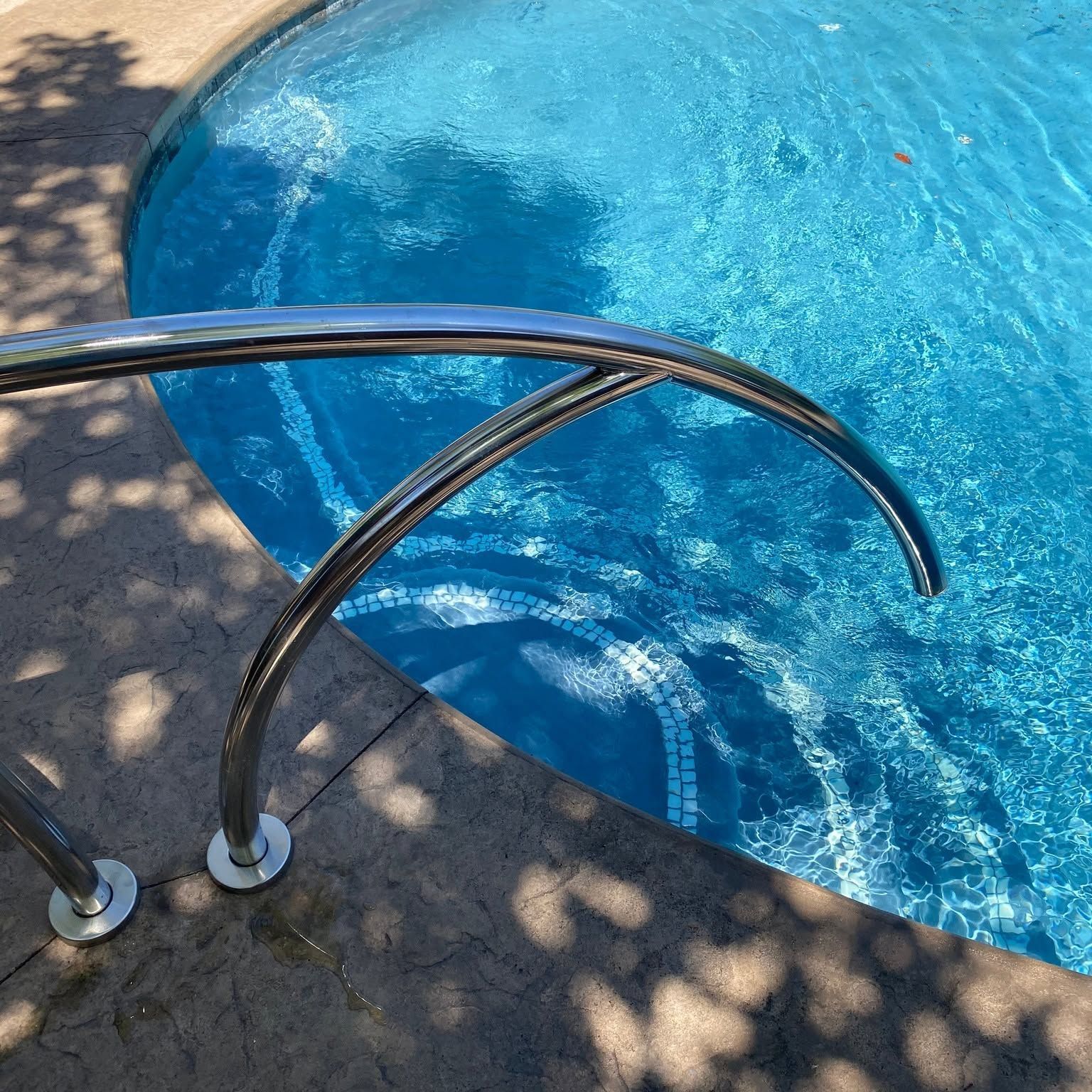 Curved metal pool handrail beside a bright blue swimming pool with sunlit water.