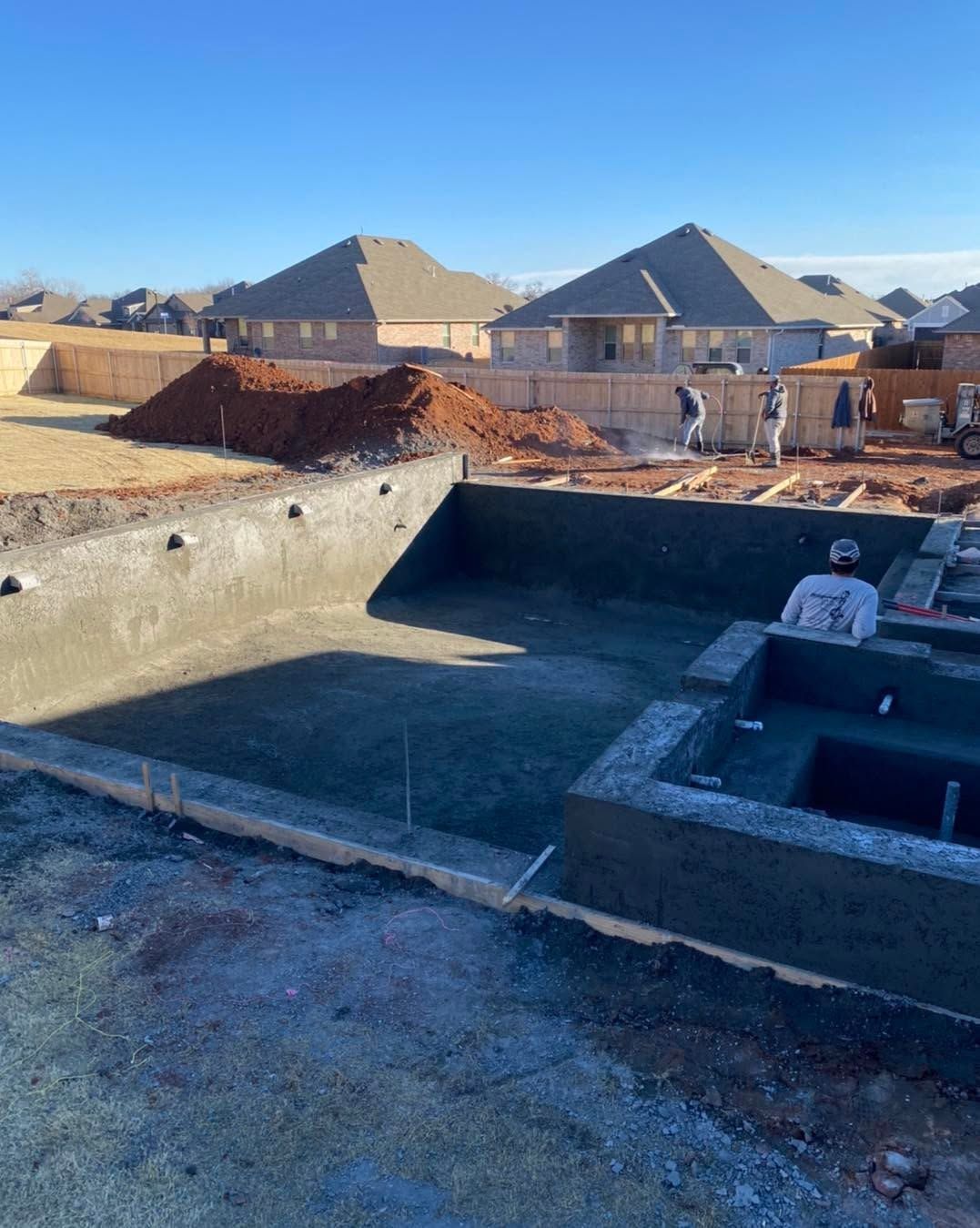 Concrete foundation under construction in a suburban neighborhood, with a worker in the pit.