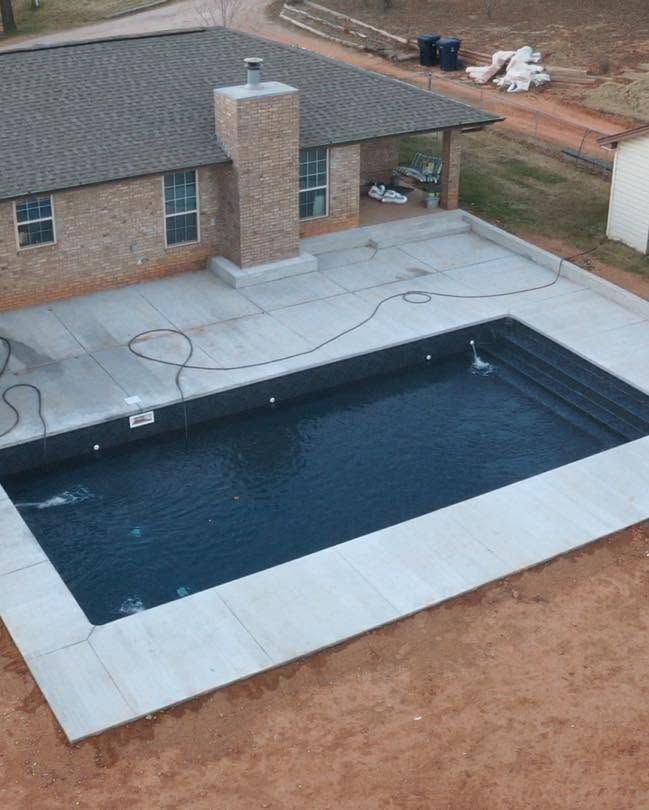 Backyard patio with a rectangular in-ground pool beside a brick house