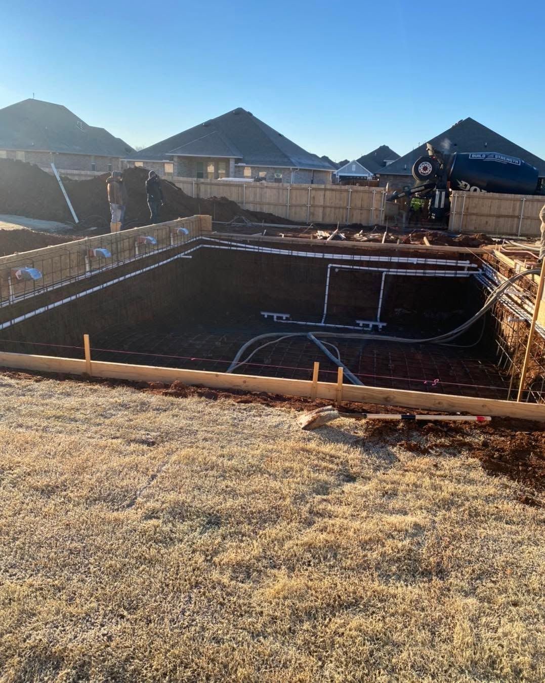 Backyard construction site with a large rectangular excavated pool shell and fenced edges under a clear sky