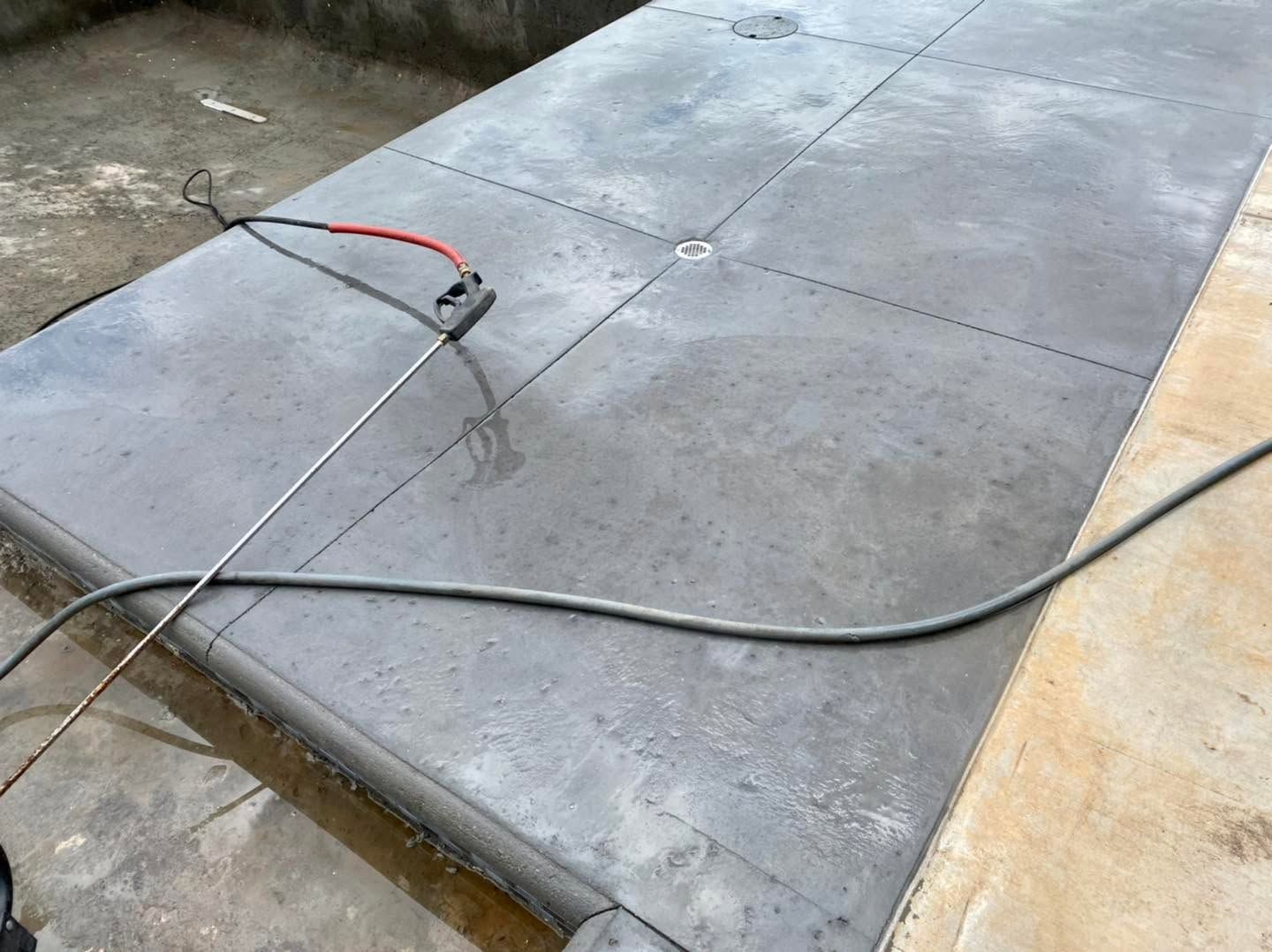 Concrete slab with a red cable and a black hose lying across a wet pavement surface