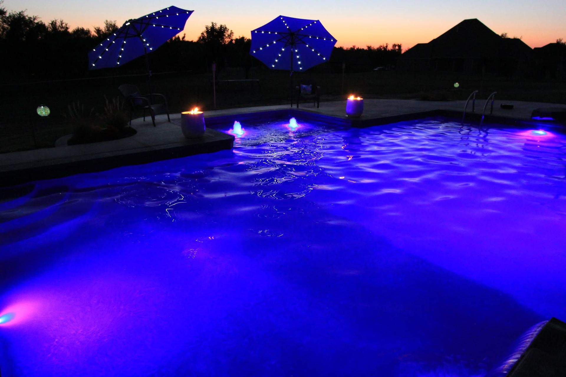 Blue-lit swimming pool at dusk with patio umbrellas and lanterns silhouetted in the background