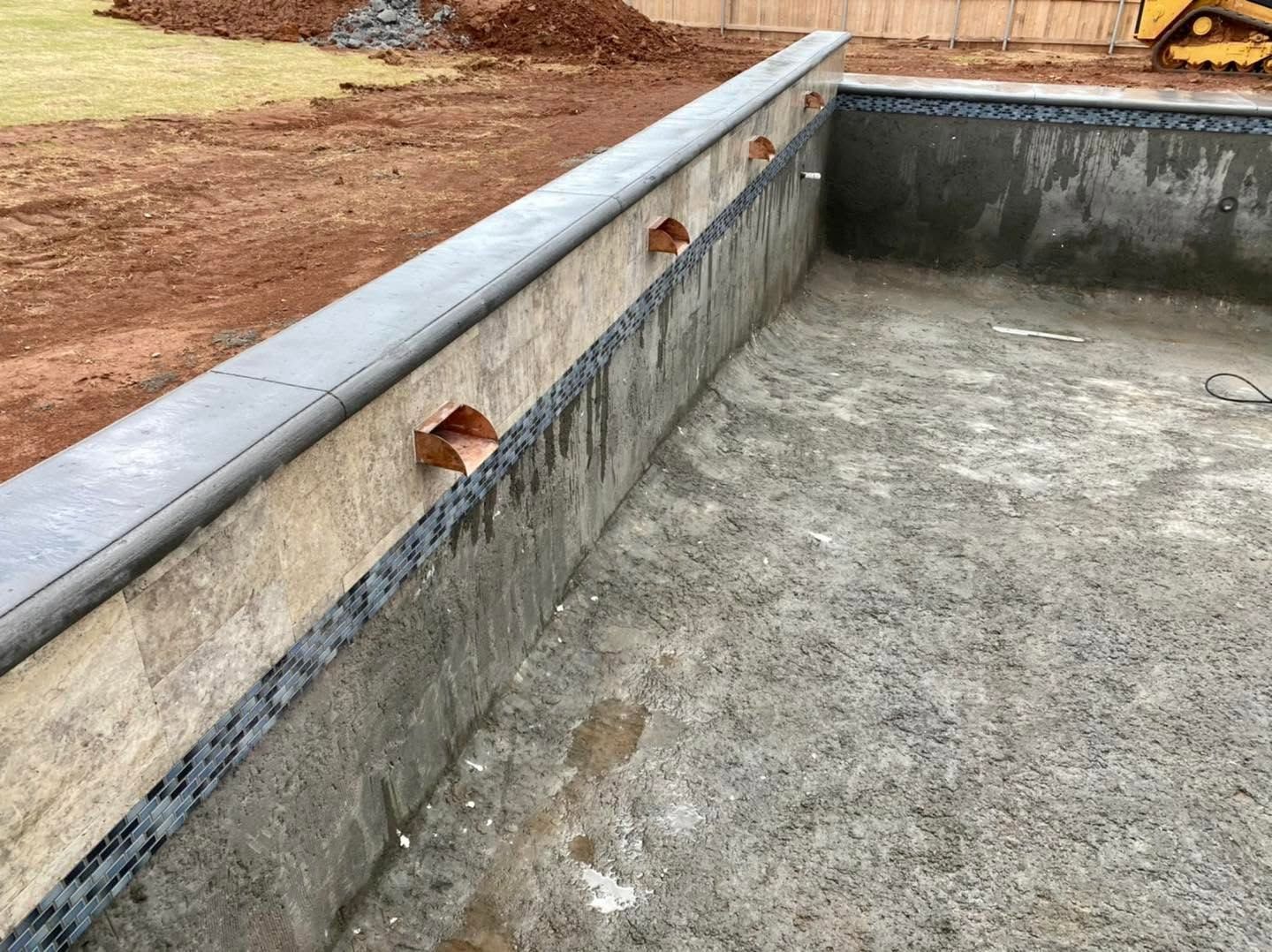 Empty concrete pool with a tiled edge and a few small openings along the side.