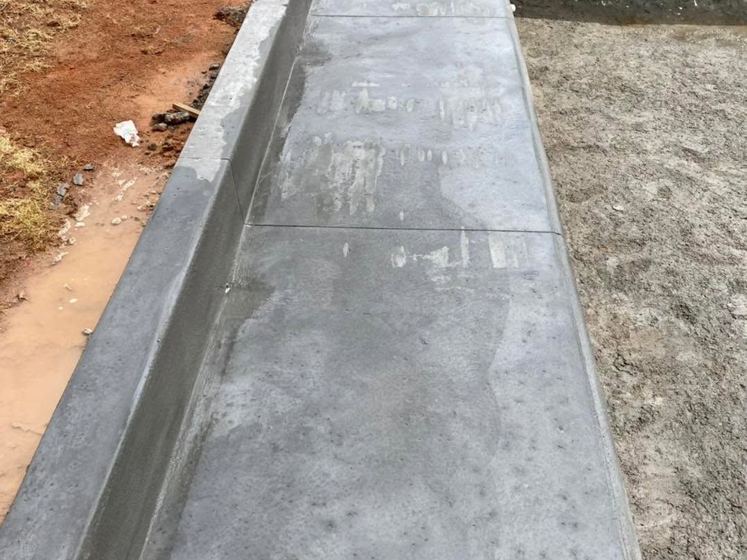 Freshly poured gray concrete curb or drainage channel along a dirt roadside