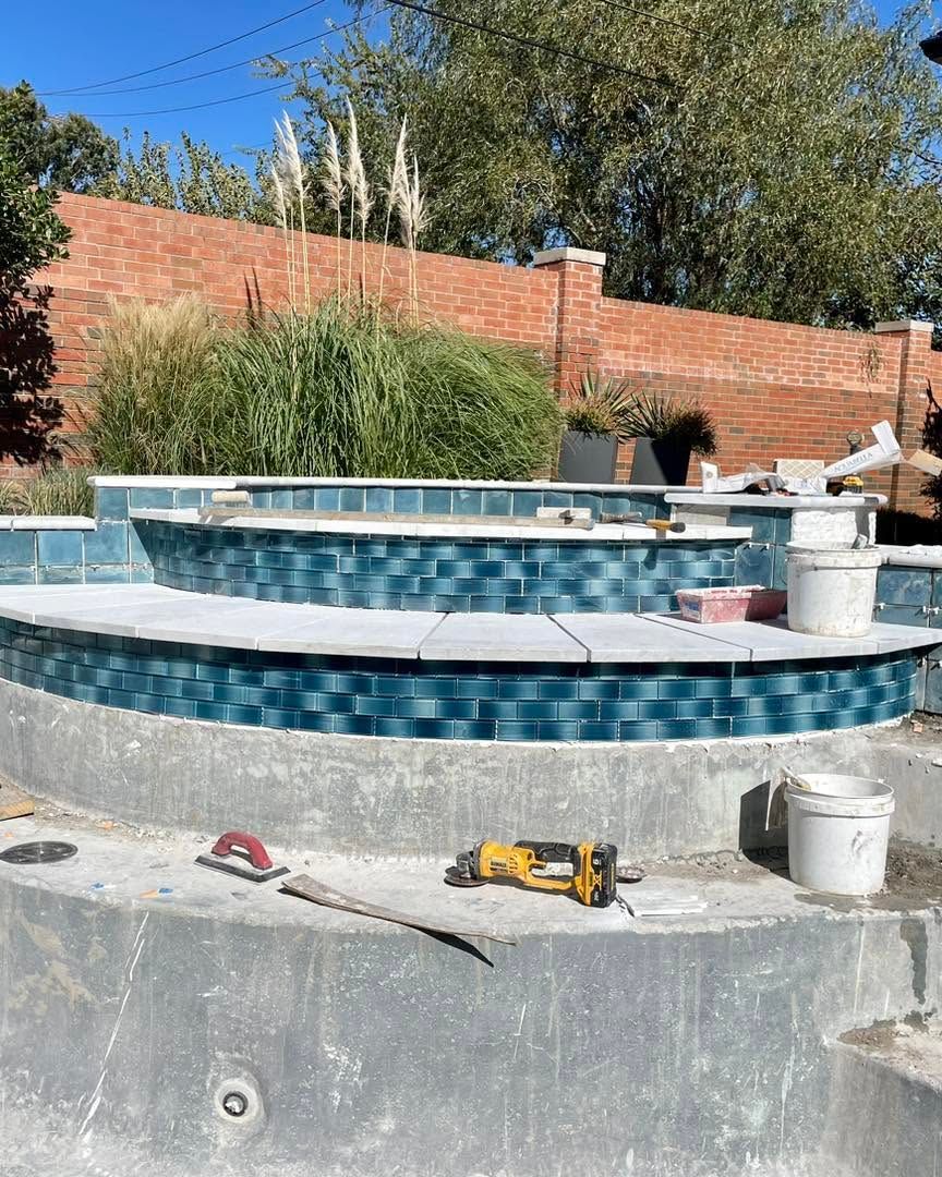 Empty backyard pool under construction with blue tile, tools, and a brick wall in the background