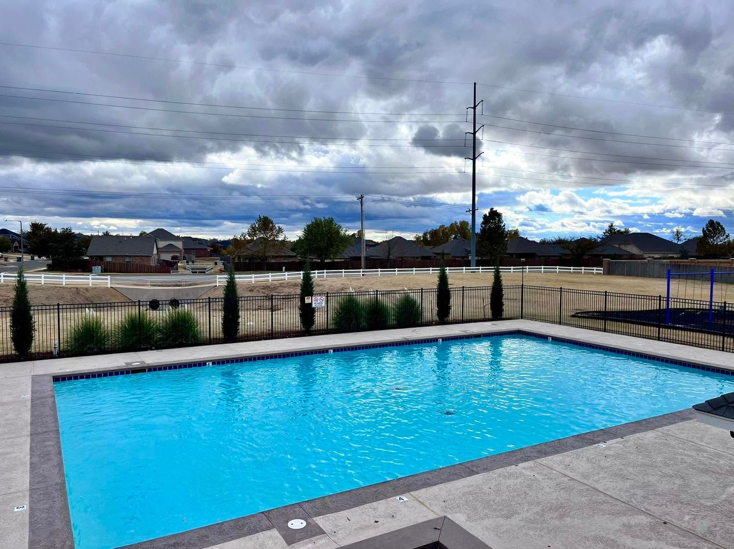Outdoor swimming pool with bright blue water beside a gray deck under a cloudy sky