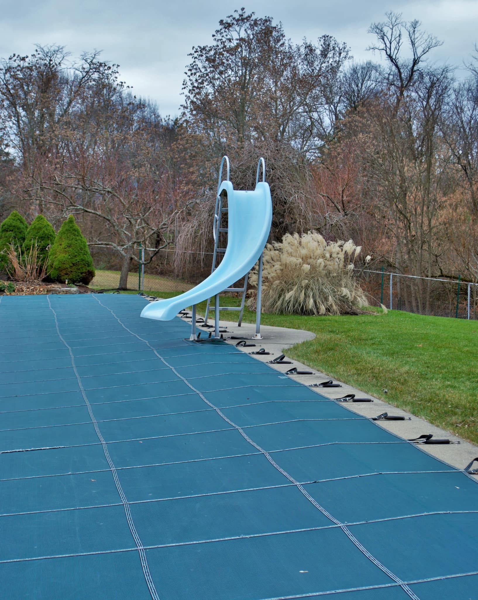 Blue playground slide on a blue padded surface in a park with trees and grass in the background