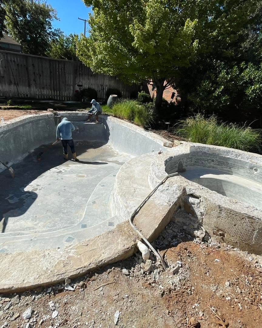 Empty drained pool with a child walking inside, surrounded by trees and a fenced yard.