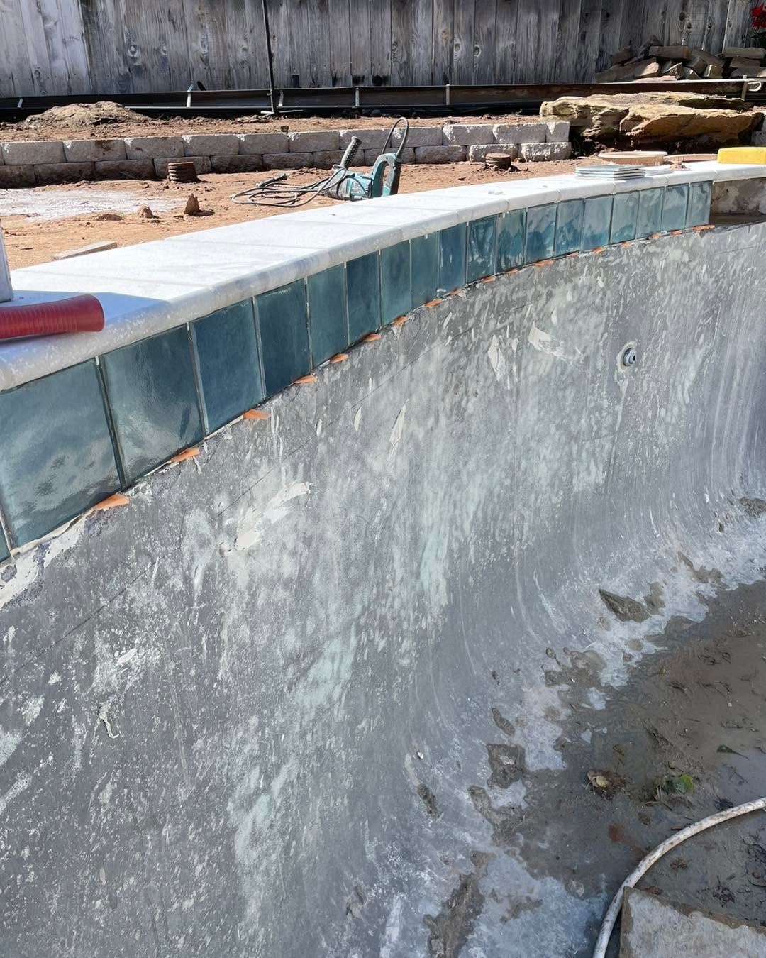 Empty concrete pool with blue tile border and weathered wall in an outdoor yard