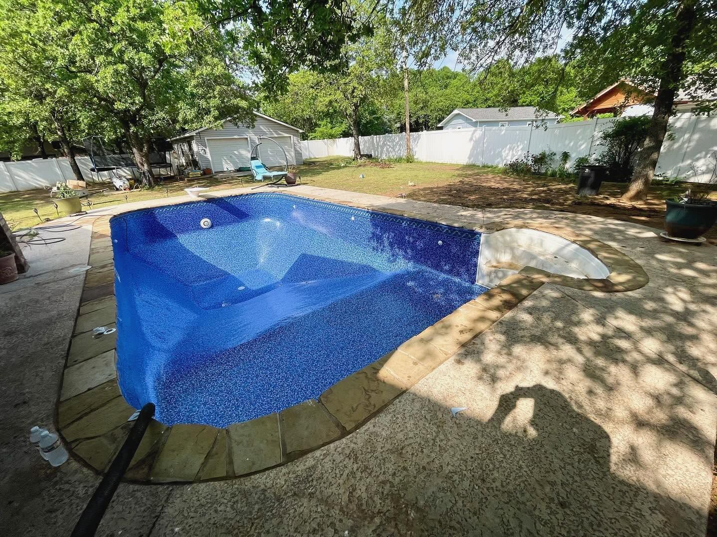 Backyard swimming pool with blue mosaic tiles, stone coping, and trees casting shade nearby