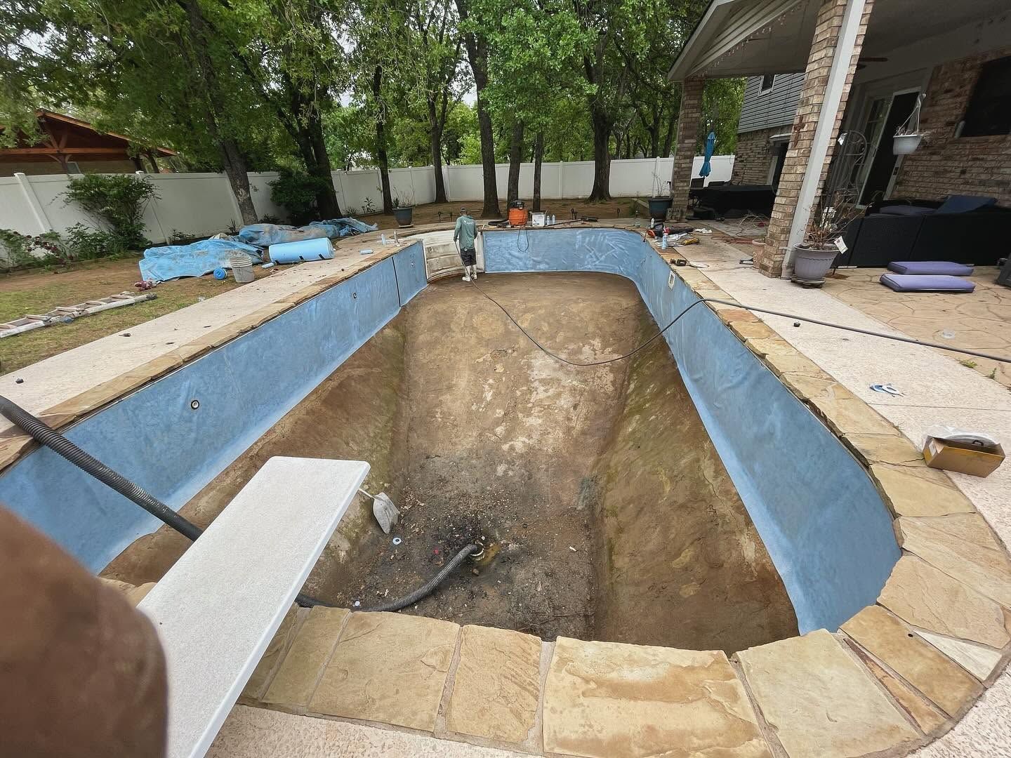 Empty backyard swimming pool under renovation, with blue-painted sides and a dirt bottom.