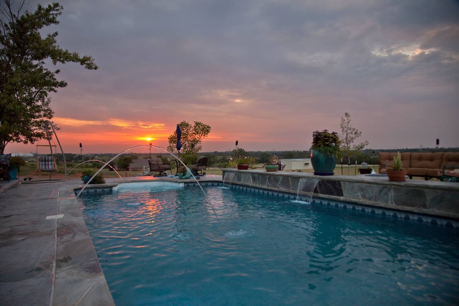 Pool at sunset with orange sky, calm water, and a resort-like patio overlooking the horizon
