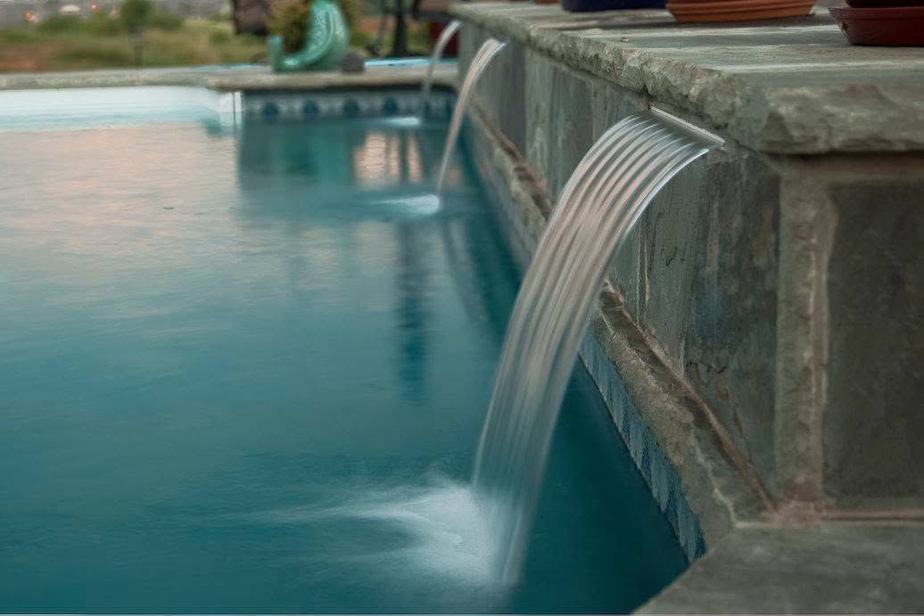 Outdoor pool with a curved stone waterfall spilling into blue water