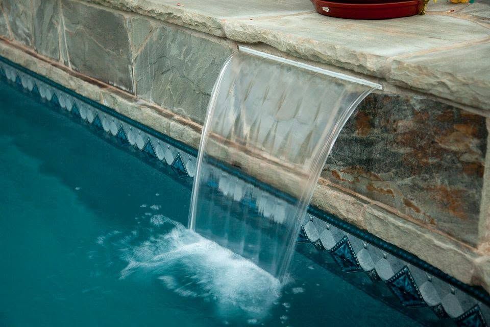 Pool waterfall spilling into blue water from a stone ledge