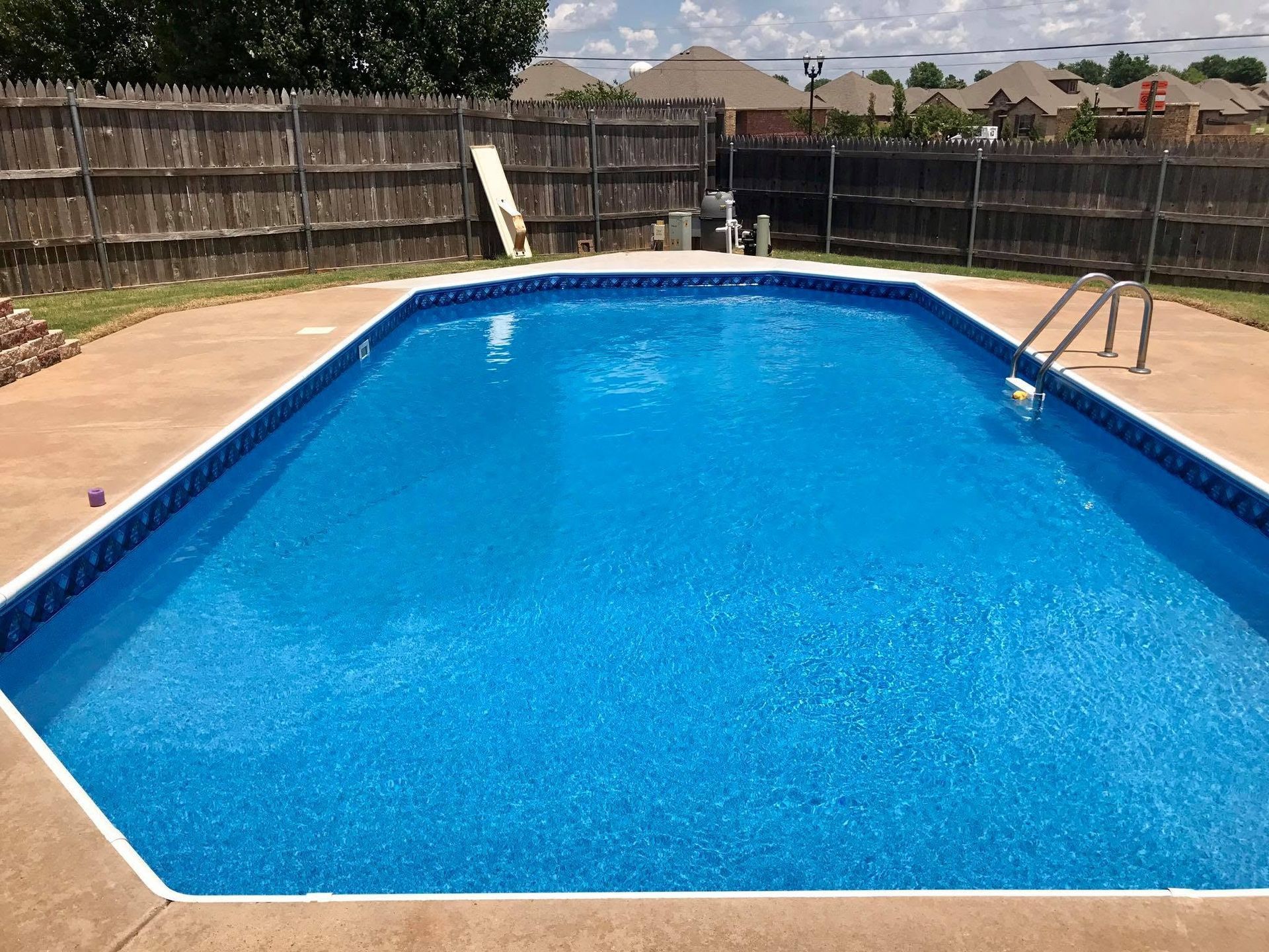 Backyard swimming pool with clear blue water, wooden fence, and patio decking on both sides
