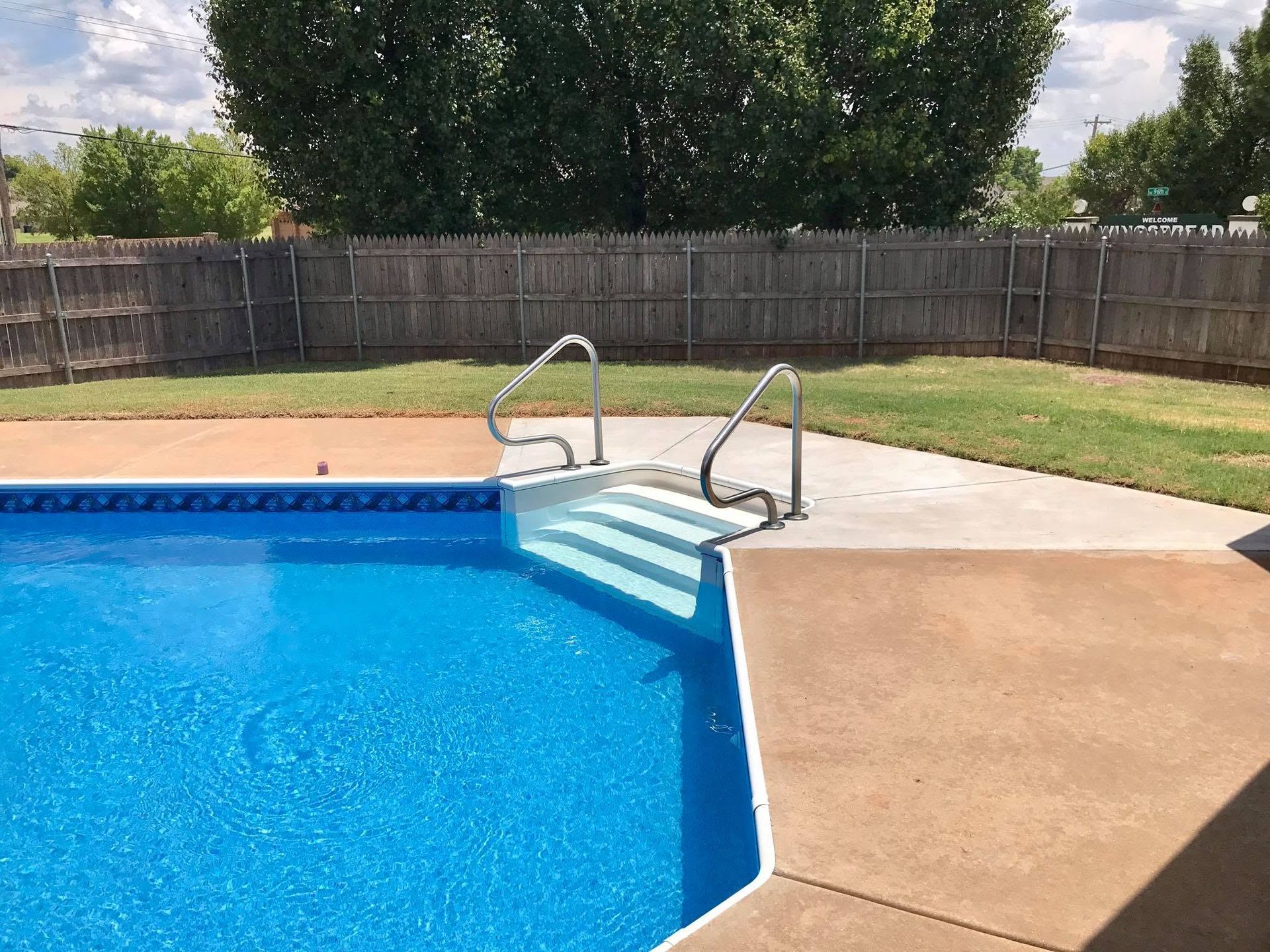 Backyard swimming pool with blue water, white steps, metal handrails, and a concrete deck.