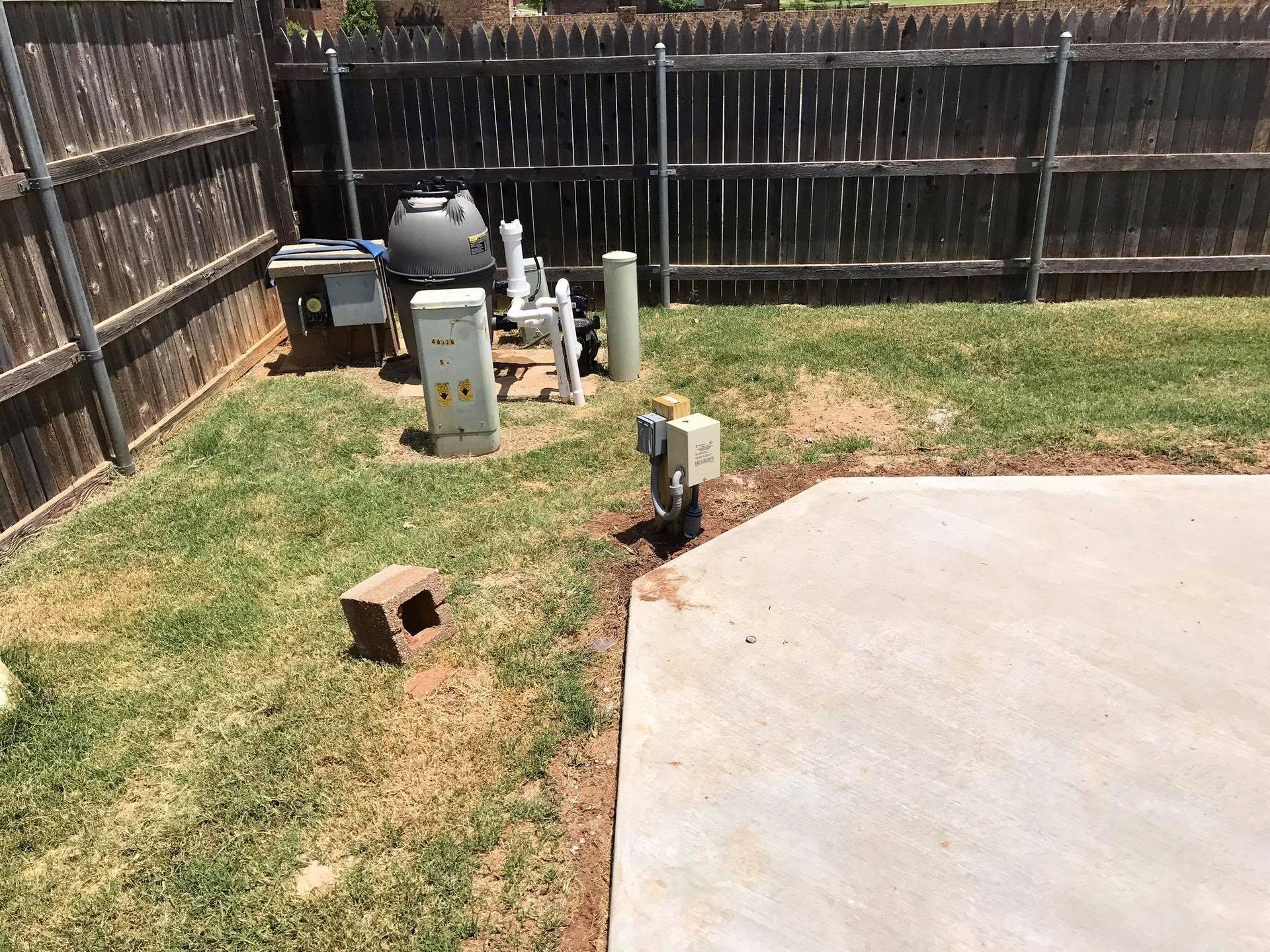 Backyard with a grill, utility equipment, fence, and a concrete patio beside patchy grass