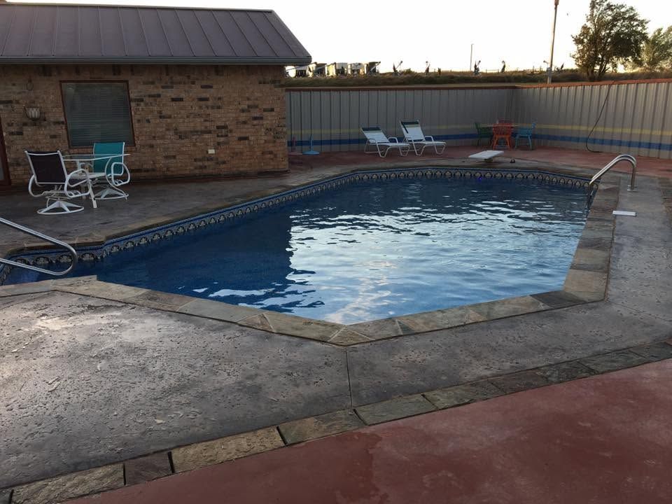 Backyard swimming pool beside a brick building, with lounge chairs and a concrete patio at dusk
