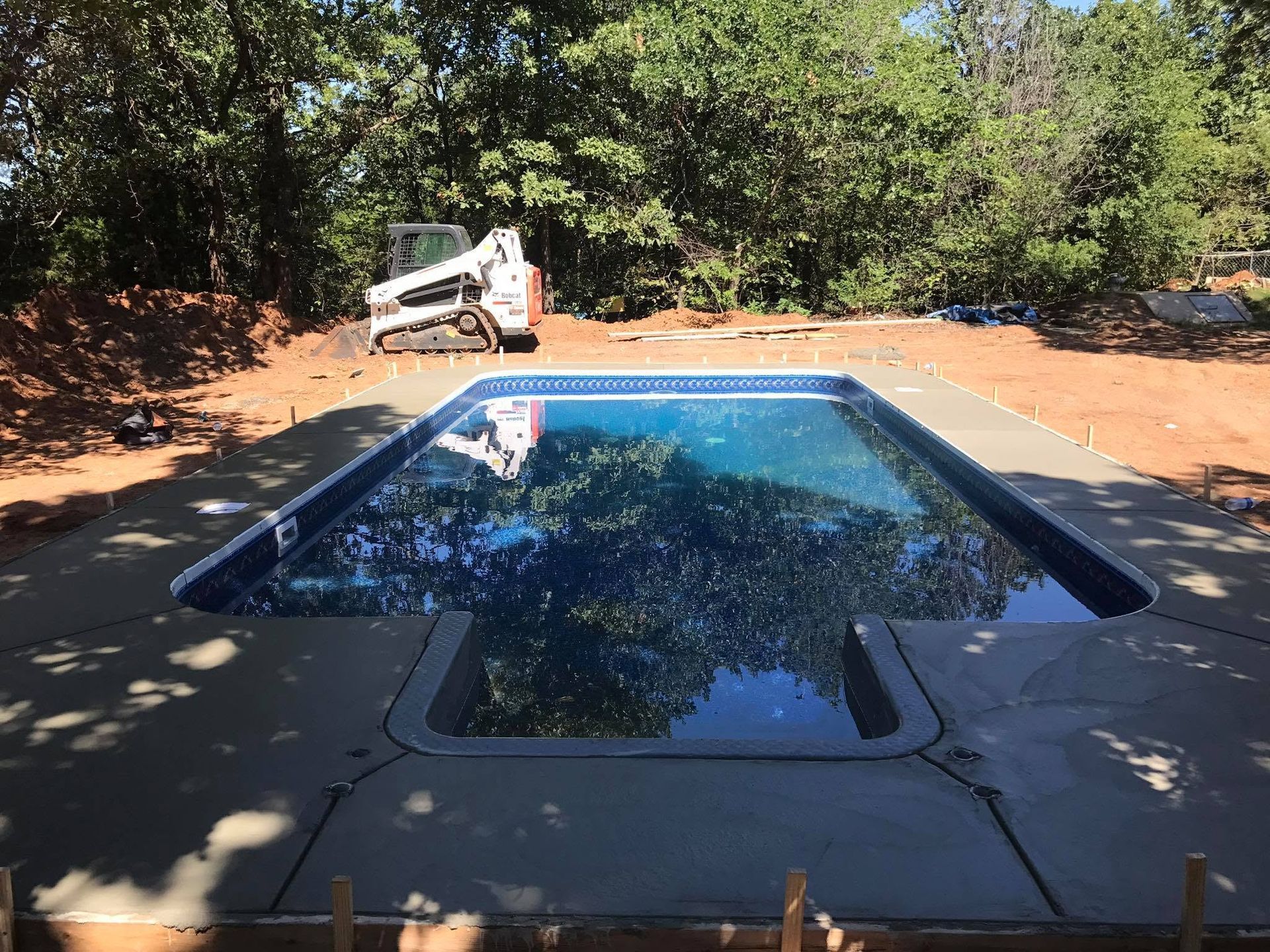 Pool in a red dirt yard with a white utility truck in the background under trees.