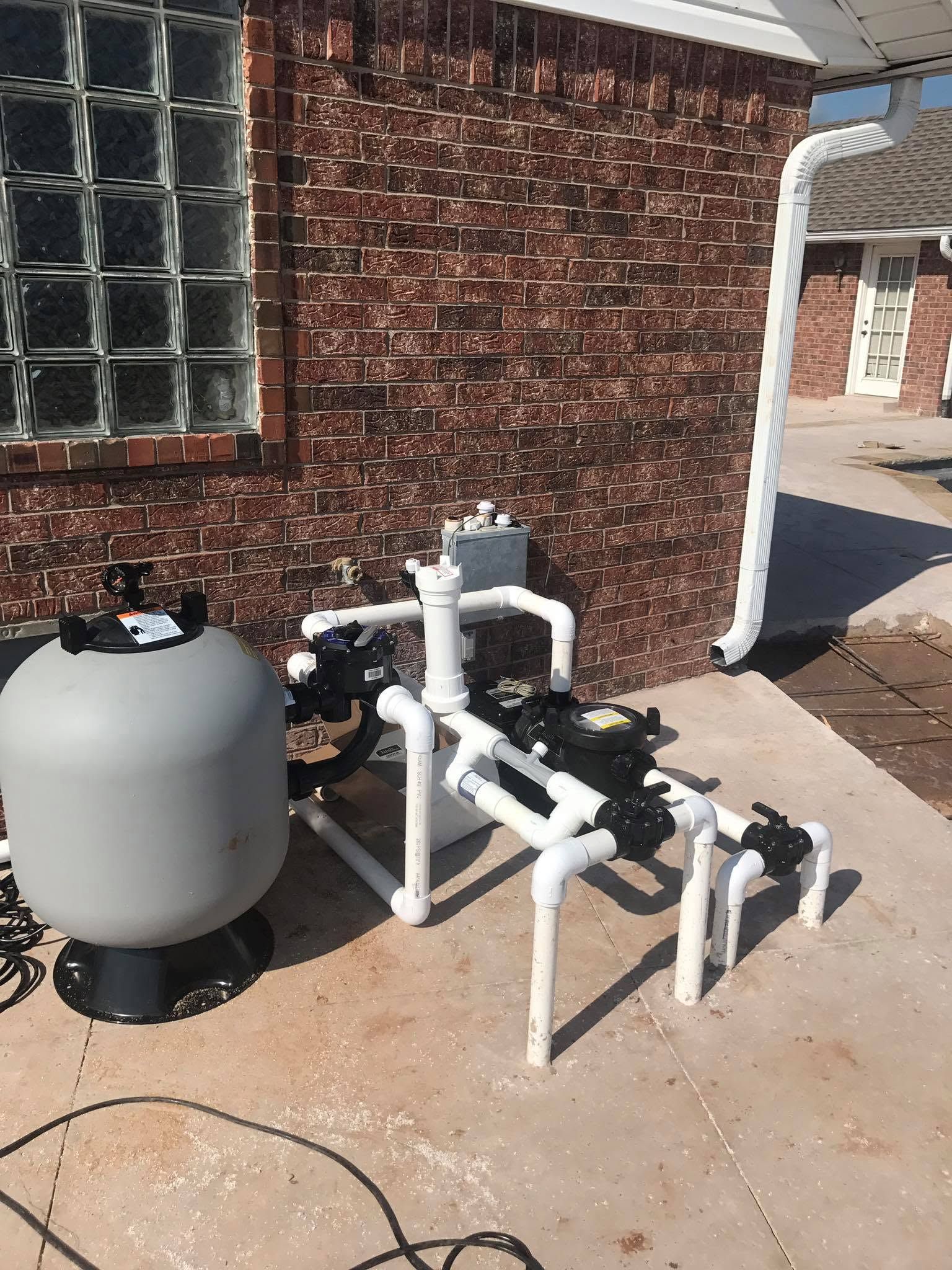 Outdoor pool equipment with white pipes and a gray tank beside a brick house