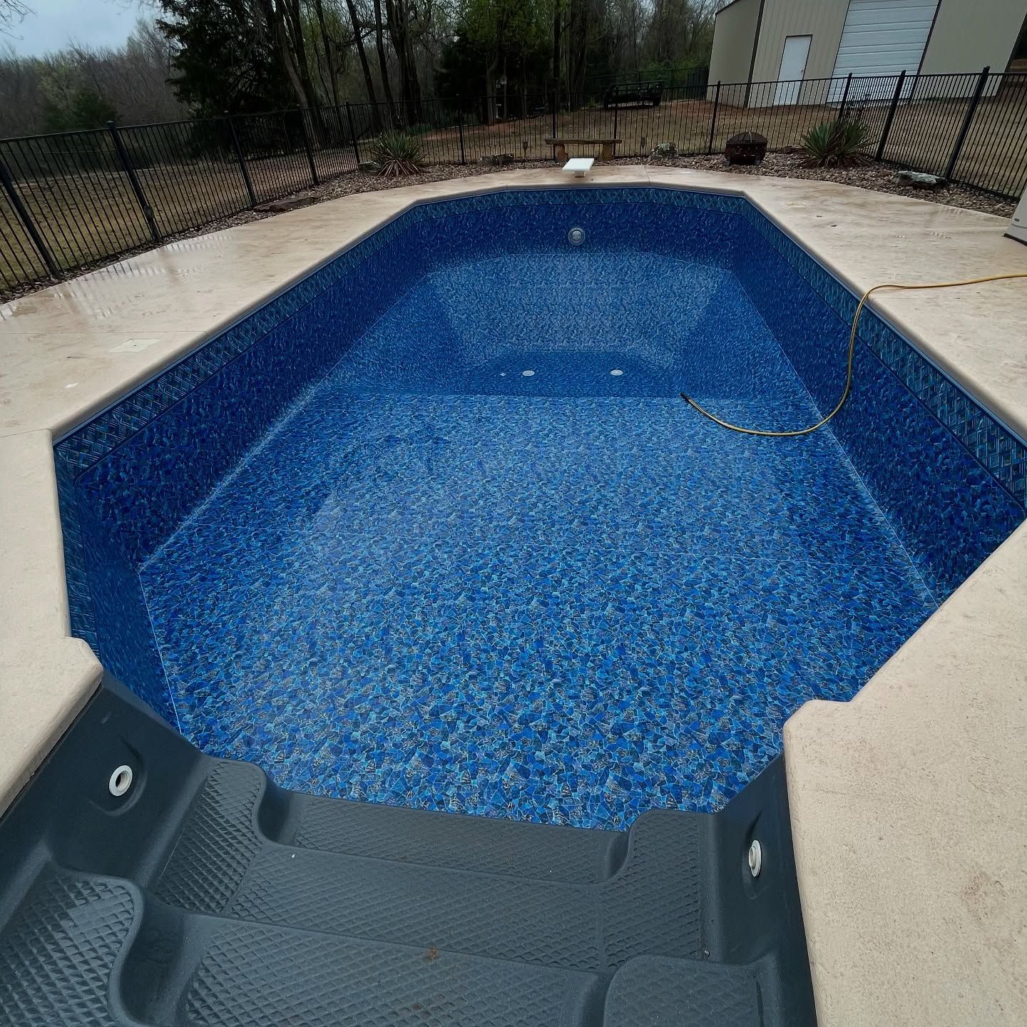 Empty blue backyard pool with surrounding concrete patio and a hose on the edge
