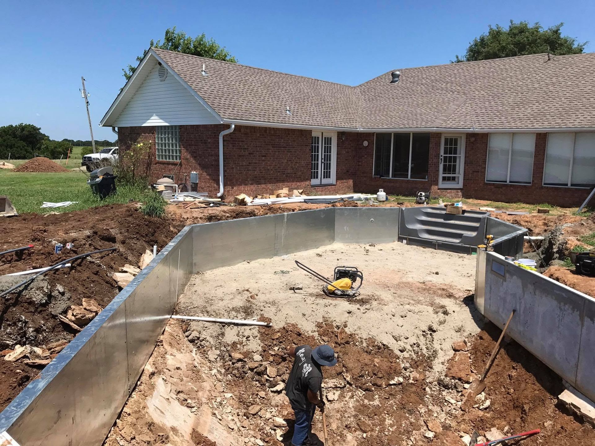 Backyard under construction with a curved concrete pool shell beside a brick house