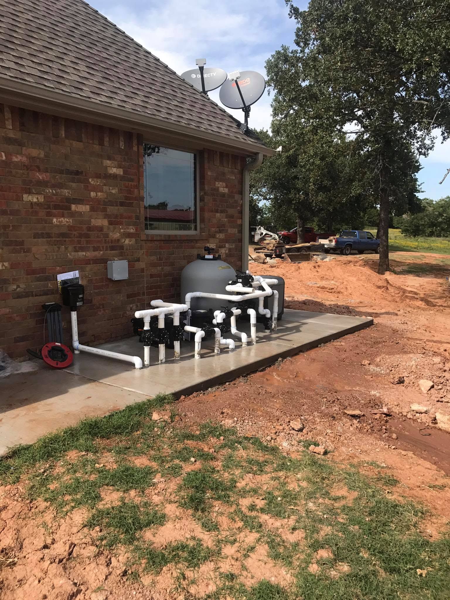 Backyard utility area beside brick house with water treatment equipment and satellite dish nearby