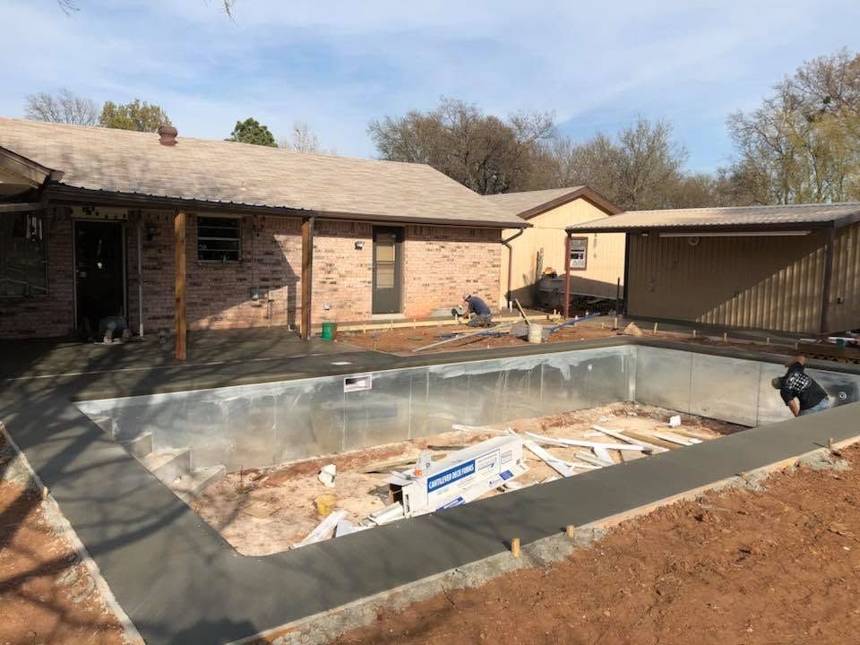 Backyard with an empty in-ground pool under construction beside a brick house and covered patio