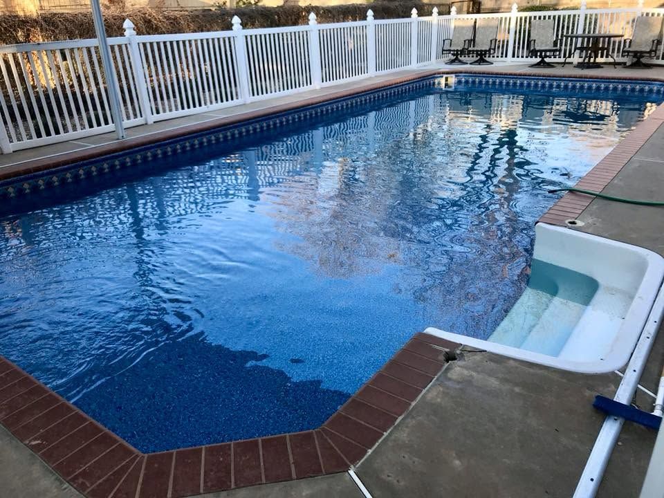 Rectangular backyard swimming pool with blue water, white fence, and concrete deck area