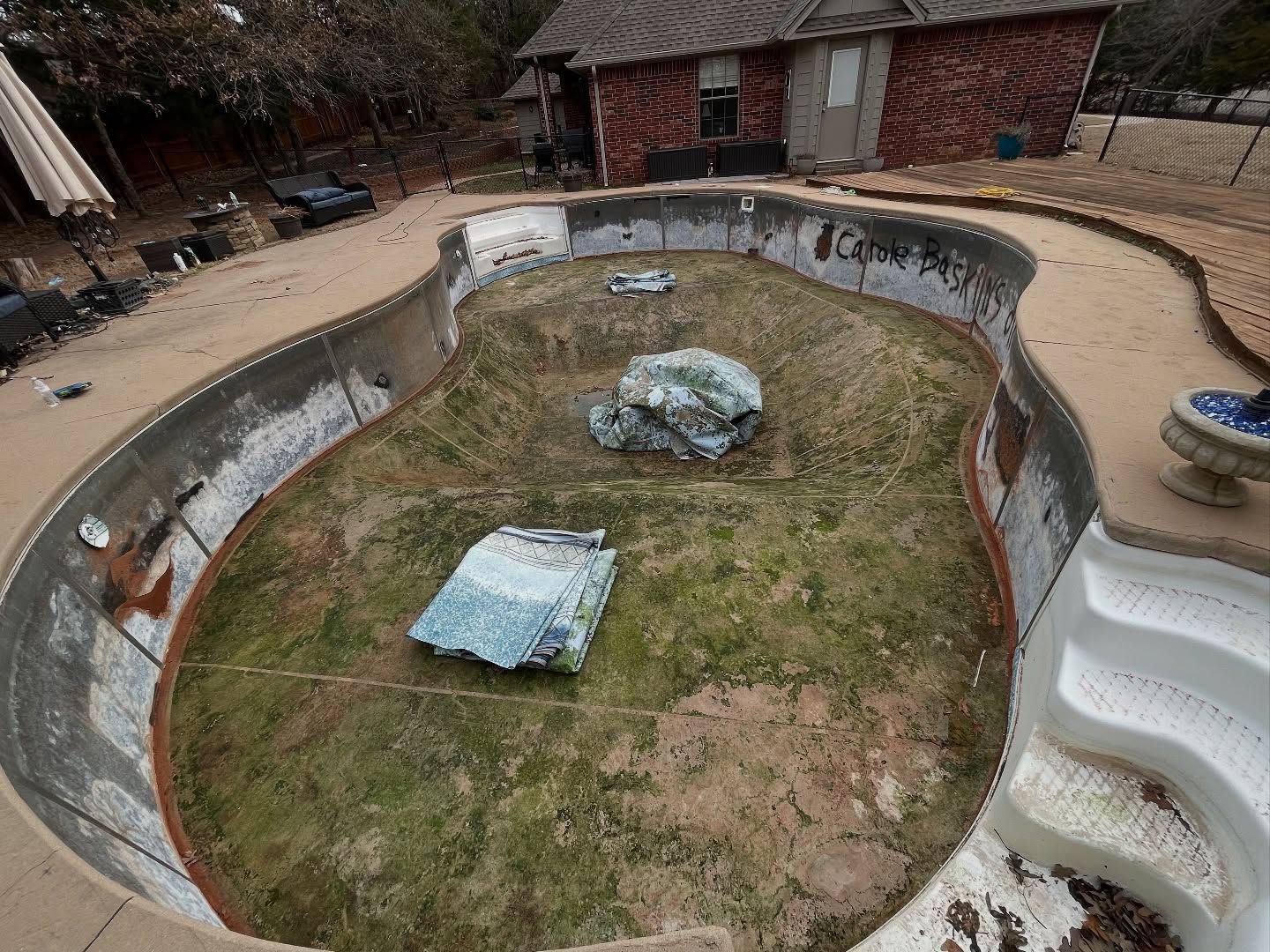 Empty backyard swimming pool under construction, with dirt, debris, and exposed concrete walls.