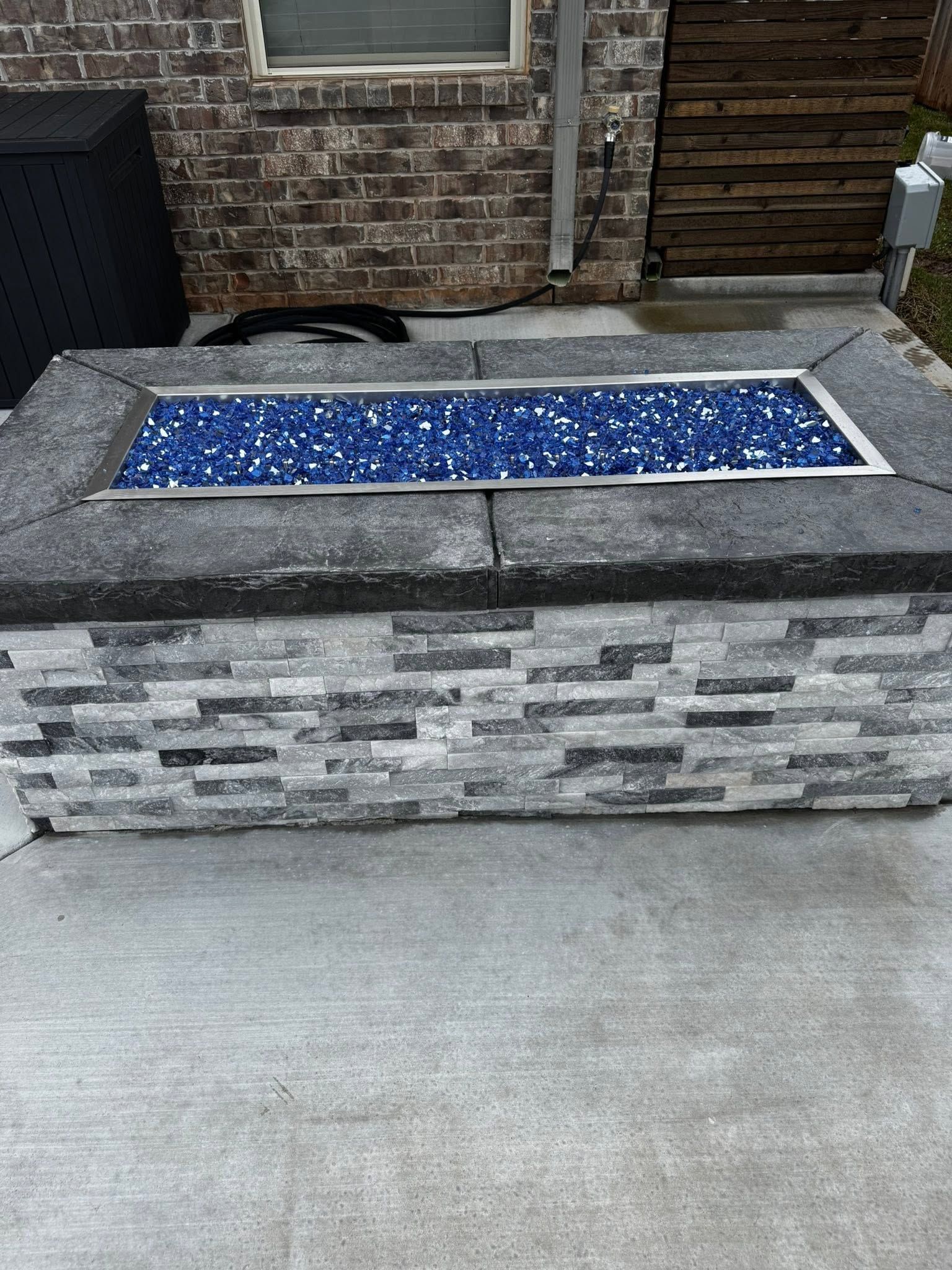 Outdoor stone water feature with blue mosaic top on a patio near a brick wall