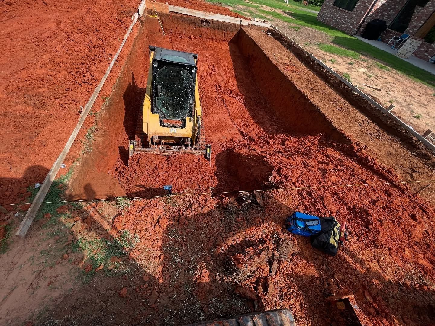 Bulldozer in a large red dirt excavation pit with a worker in blue nearby