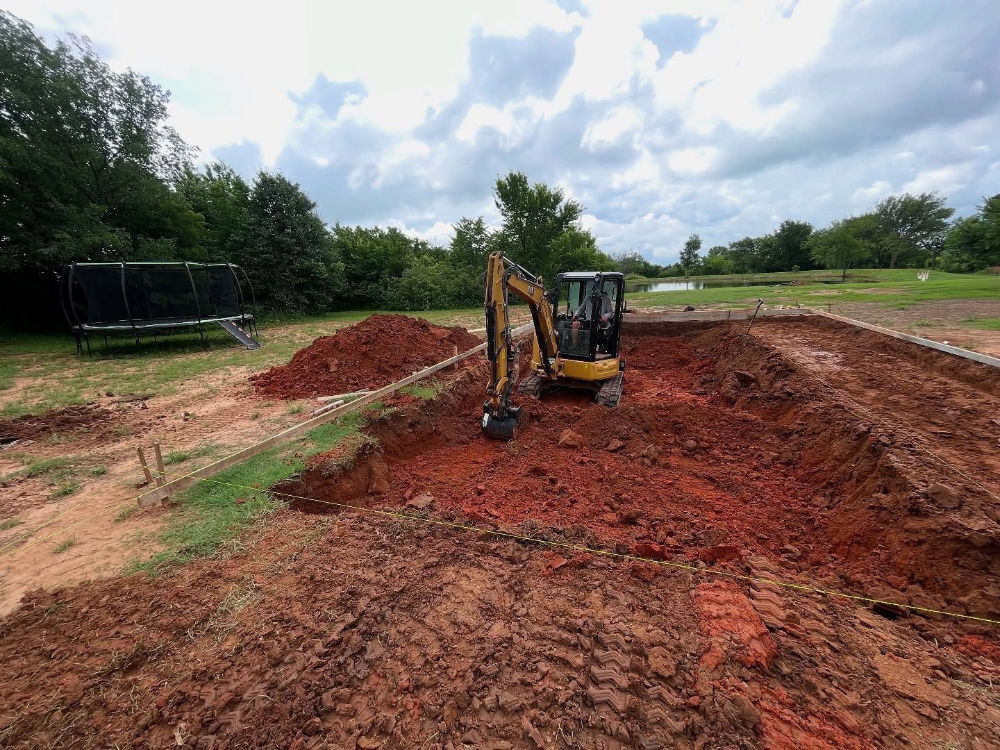 Excavator working on a red dirt construction site under a cloudy sky