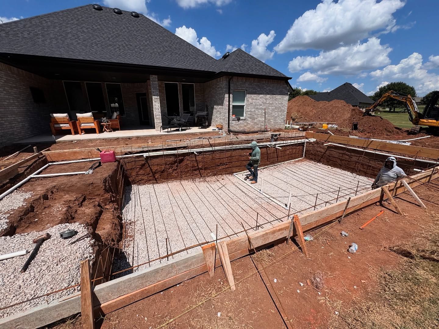 Construction site with concrete foundation forms beside a dark-roofed house under construction