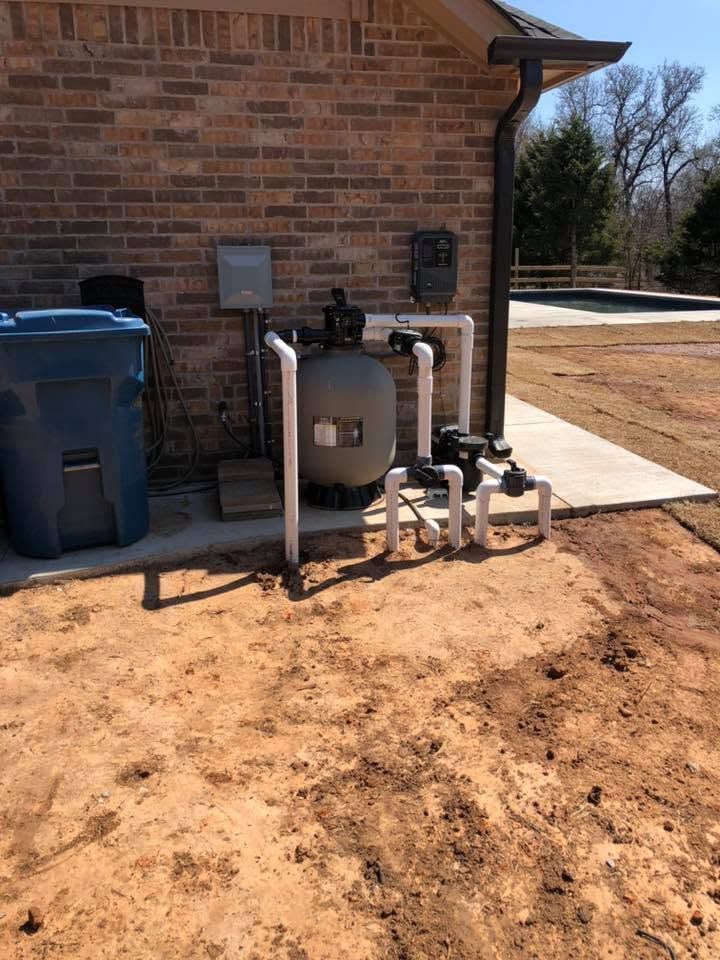 Outdoor house side yard with utility tanks, pipes, and blue bins against a brick wall.