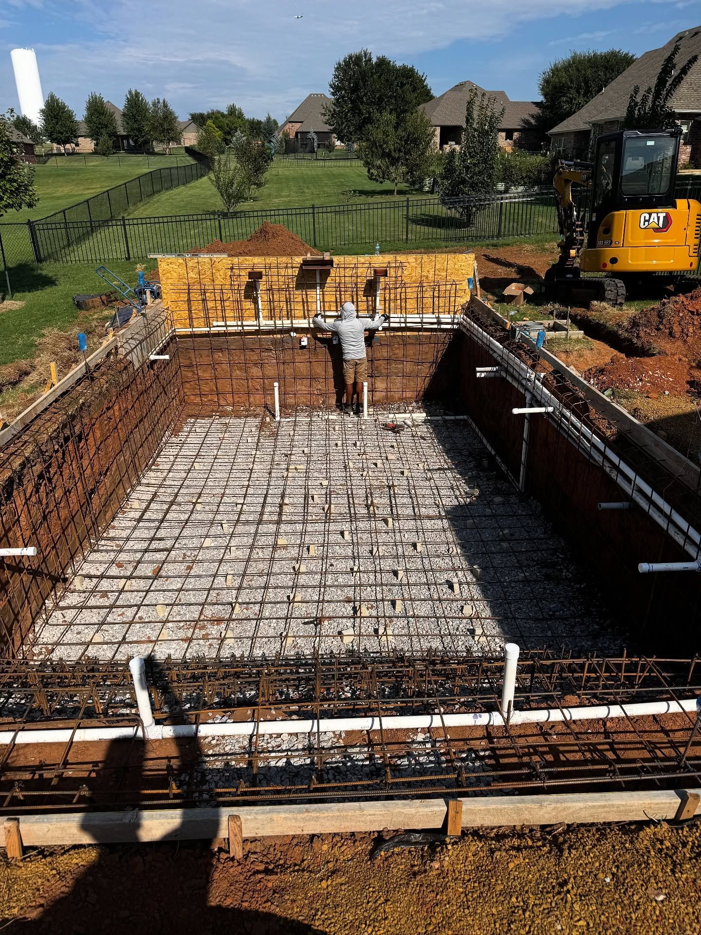 Foundation excavation with rebar and concrete forms at a construction site, with a yellow excavator nearby.