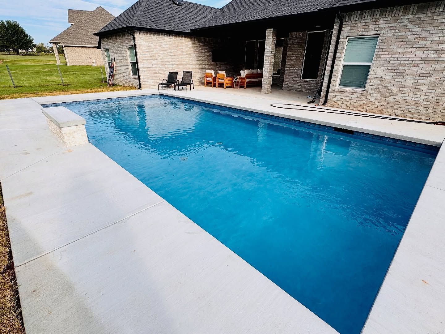 Backyard swimming pool beside a stone house with a covered patio and lounge chairs